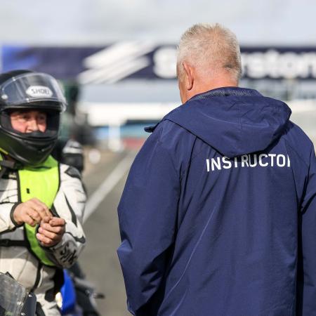 Instructor in conversation with a rider at Silverstone. Gantry displaying Silverstone logo is on display in the background. 