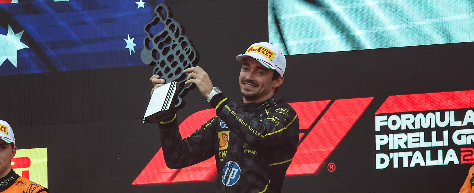 Charles leclerc stands on the top step of the podium holding the trophy and smiling to the crowd