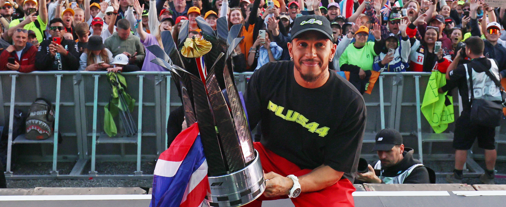 Sir Lewis Hamilton poses with the Silverstone crowd, holding his trophy after a historic ninth win at the British Grand Prix. 
