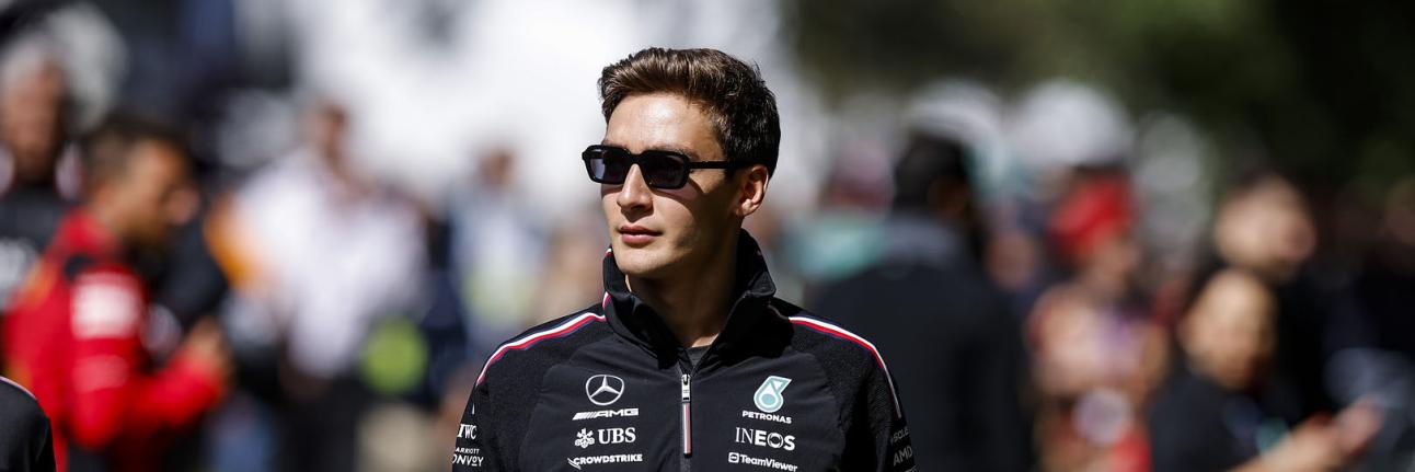 George Russell walking through a Formula 1 paddock wearing Mercedes teamwear