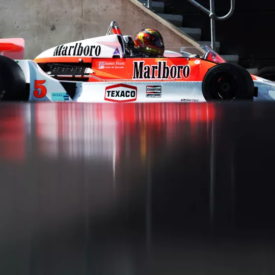 Classic F1 car drives past camera, reflecting off surface in foreground. 