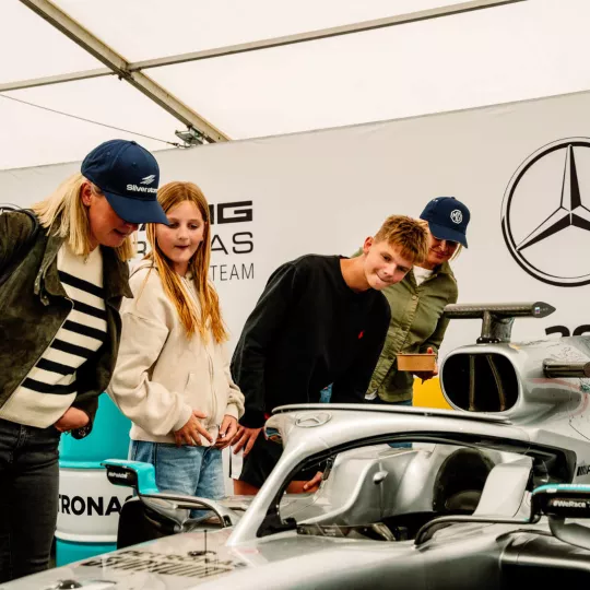 Family take a closer look at Mercedes F1 car, parked inside a tent 