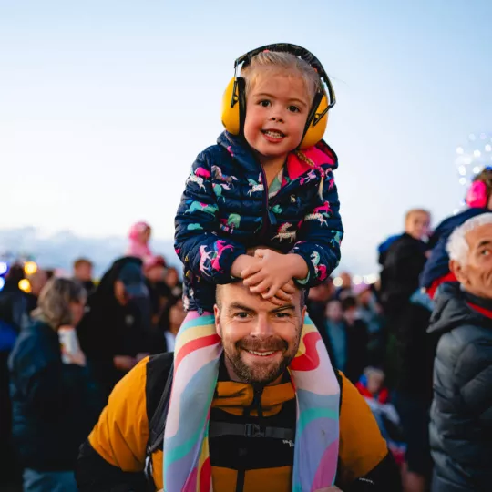 Guests enjoying concert entertainment, a child sits upon a man's shoulders