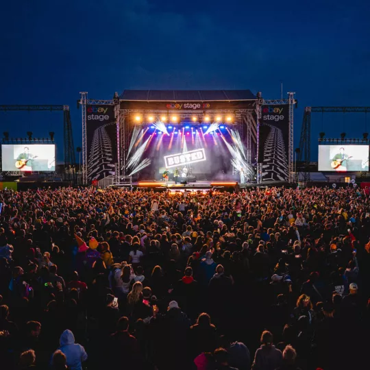 Main stage, as seen from tech tower. After dark, with lights illuminating crowd as we look towards the stage, centred. 