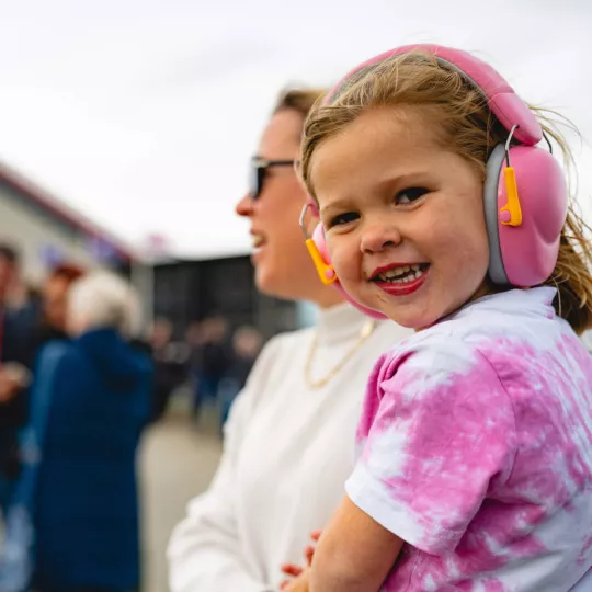 Young child wearing ear defenders smiles at the camera