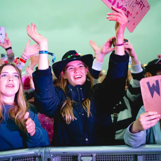 Fan in the crowd at a concert claps and waves at the mainstage artist. Front of barrier. 